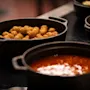 A close-up of a buffet with black pots filled with hot food, including crispy fried items and a rich red stew.