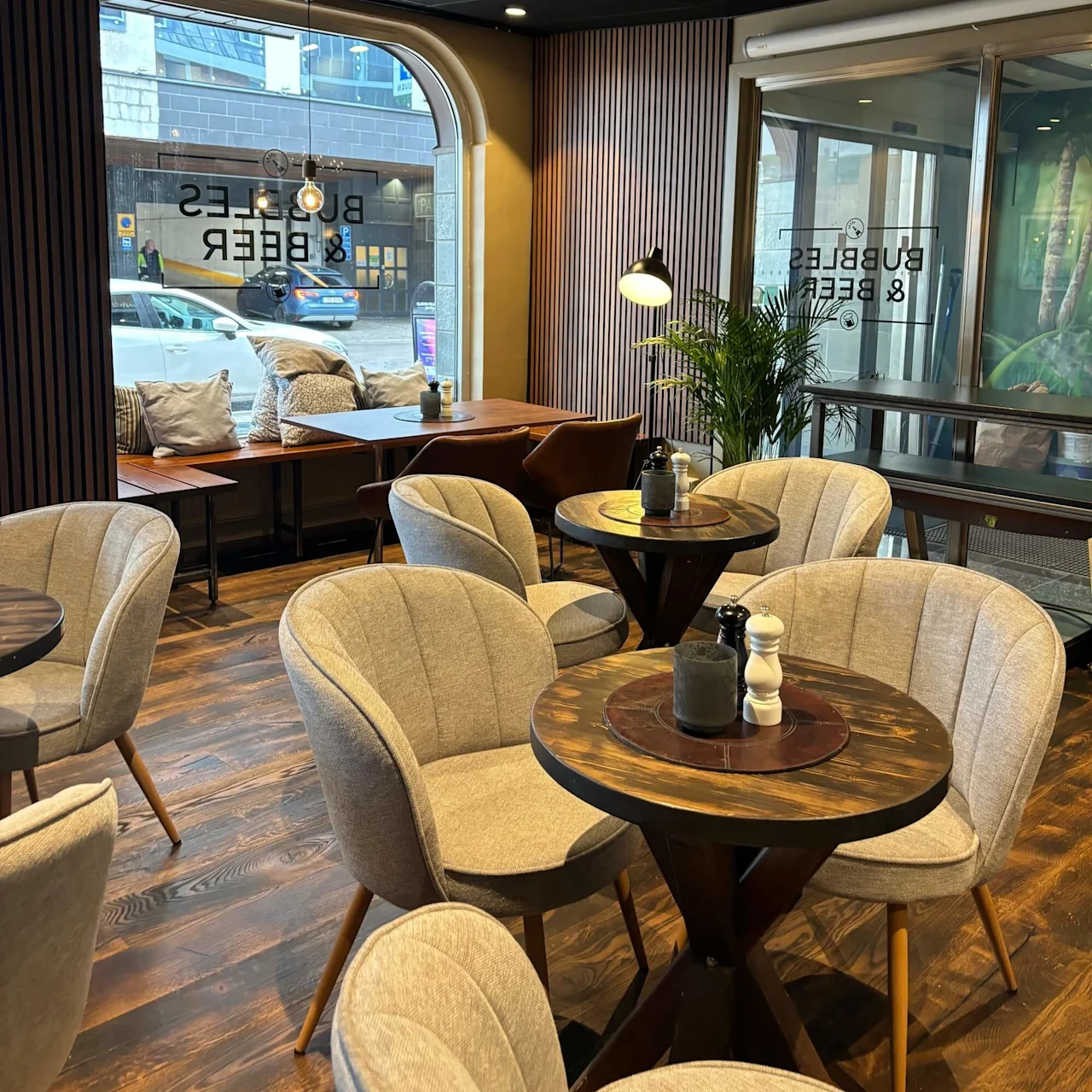 A cozy café interior with upholstered chairs, round tables, large windows overlooking a city street.