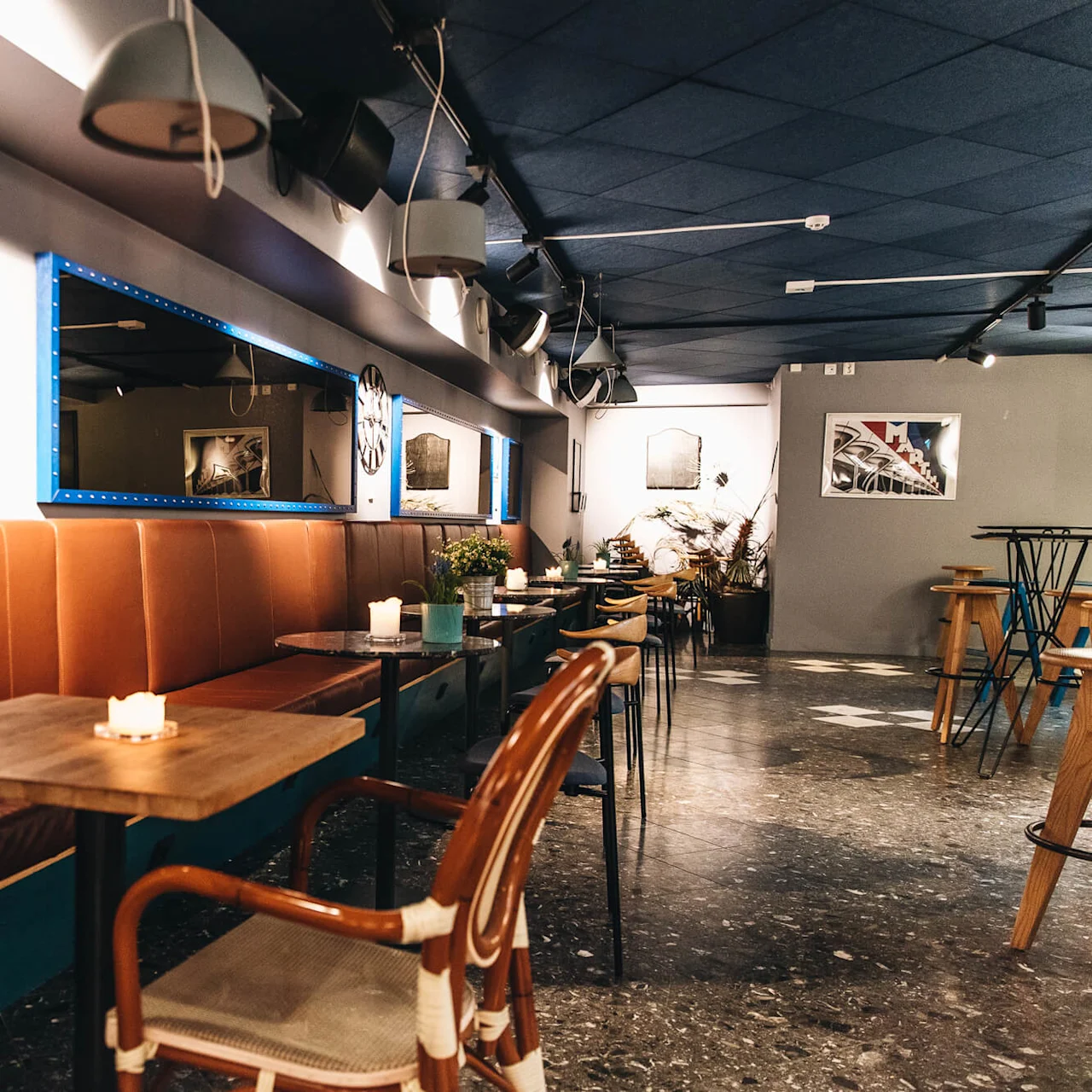 En koselig kafé med trebord, stearinlys, brune lærseter og moderne interiør. Speil med blå ramme og veggkunst fremhever den varme stemningen.