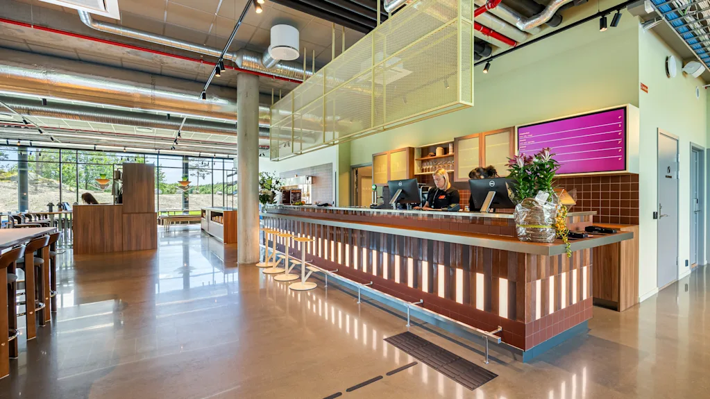 A modern and spacious hotel lobby with a long reception counter, bar stools, and large windows overlooking an outdoor area.