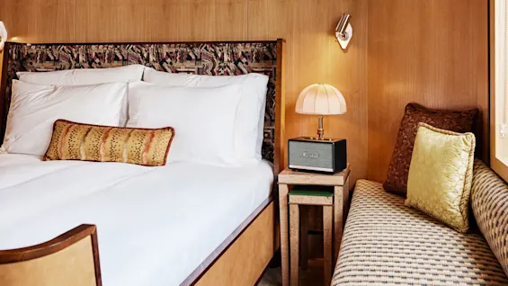Et koselig hotellrom med en elegant oppredd seng, nattbord, dekorative puter og mønstrete tekstiler, som utstråler komfort og gjestfrihet.
