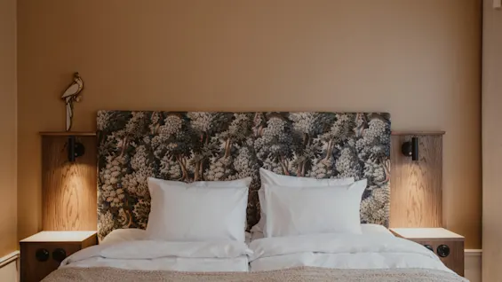 Home Hotel Baltzar - Standard Twin. A cozy bed with a forest-patterned headboard, white pillows, and warm lighting.