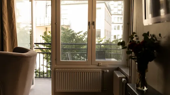 Ett inbjudande inomhusutrymme med ett stort fönster och öppen balkong, med utsikt över en stadsscen med lummiga träd.