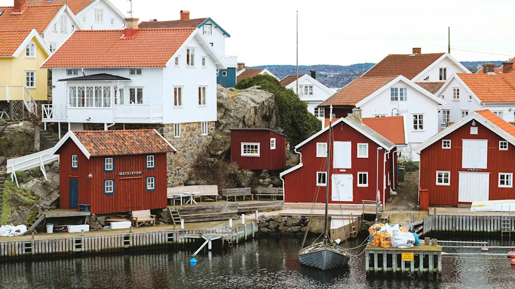 A picturesque coastal village with traditional red and white houses overlooking a calm harbor with boats and wooden docks.