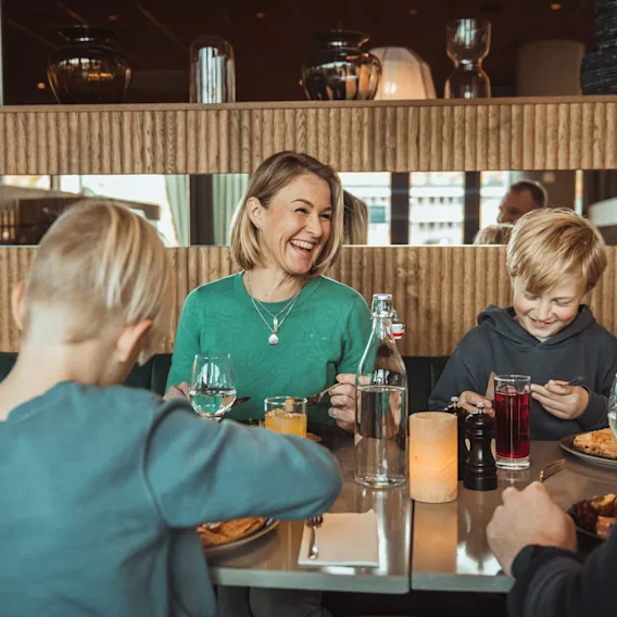 A family enjoying a happy meal together at a restaurant, with a woman laughing and children smiling.