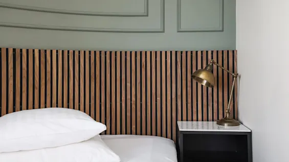 Viihtyisä makuuhuone Comfort Hotel Linköping Cityssä, jossa on sänky, puinen sängynpääty ja messinkilamppu yöpöydällä.