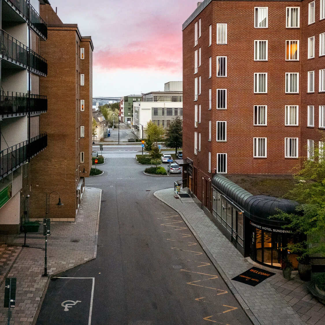 Tegelbyggnader omger en tom gata i skymningen, rosa himmel ovanför; skylten lyder "Quality Hotel Sundsvall."