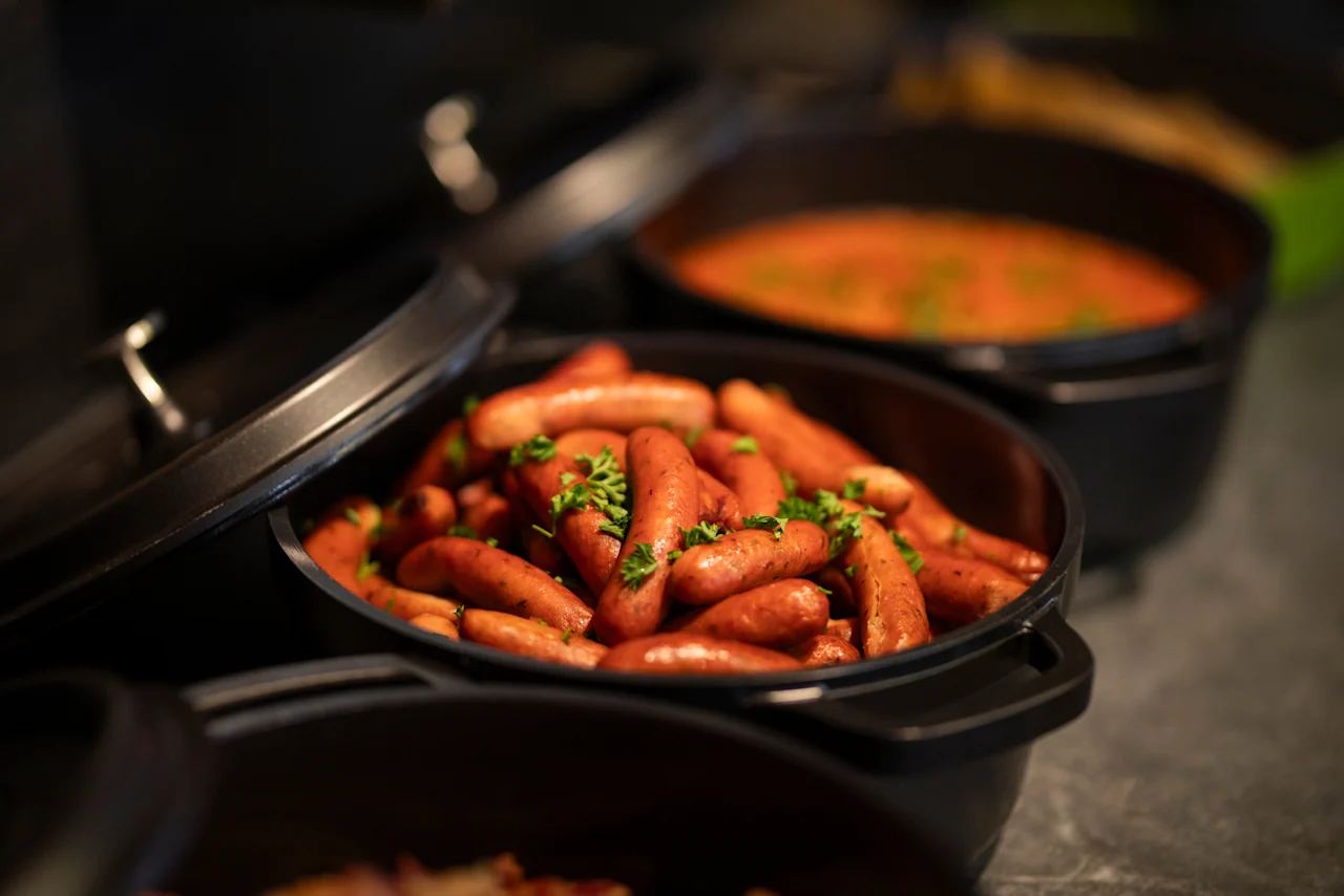 Varma korvar garnerade med färska örter i en serveringsskål, med en smakrik gryta i bakgrunden, redo för en måltid.