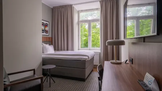 Et hyggeligt hotelværelse med en komfortabel seng, et skrivebord og et vindue med udsigt til grønne områder. Rygning forbudt skilt synligt.
