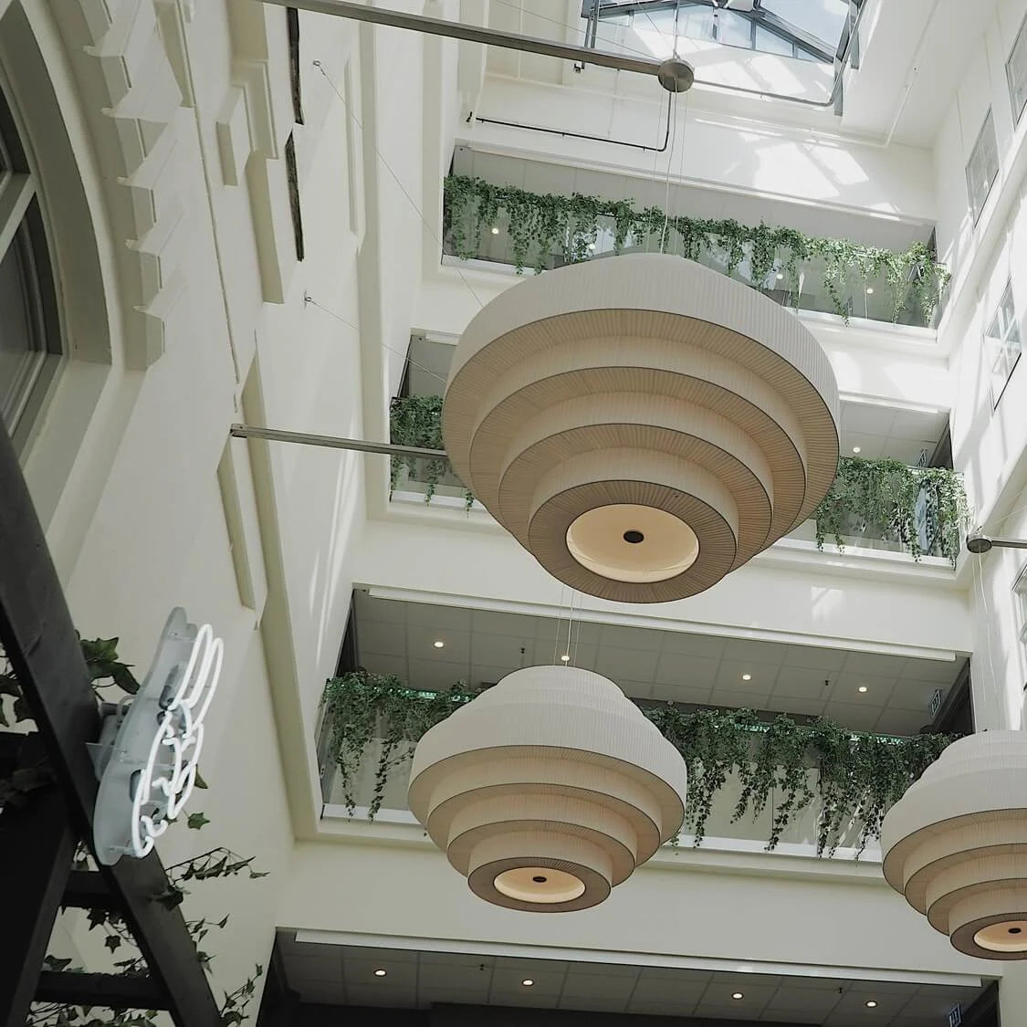 Tiered pendant lights hang from a high ceiling in a bright atrium with greenery.