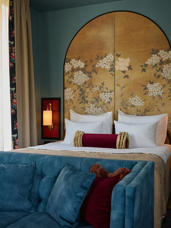 A luxurious hotel room at Hotel Christiania Teater with a large bed, floral headboard, and a comfortable blue sofa.
