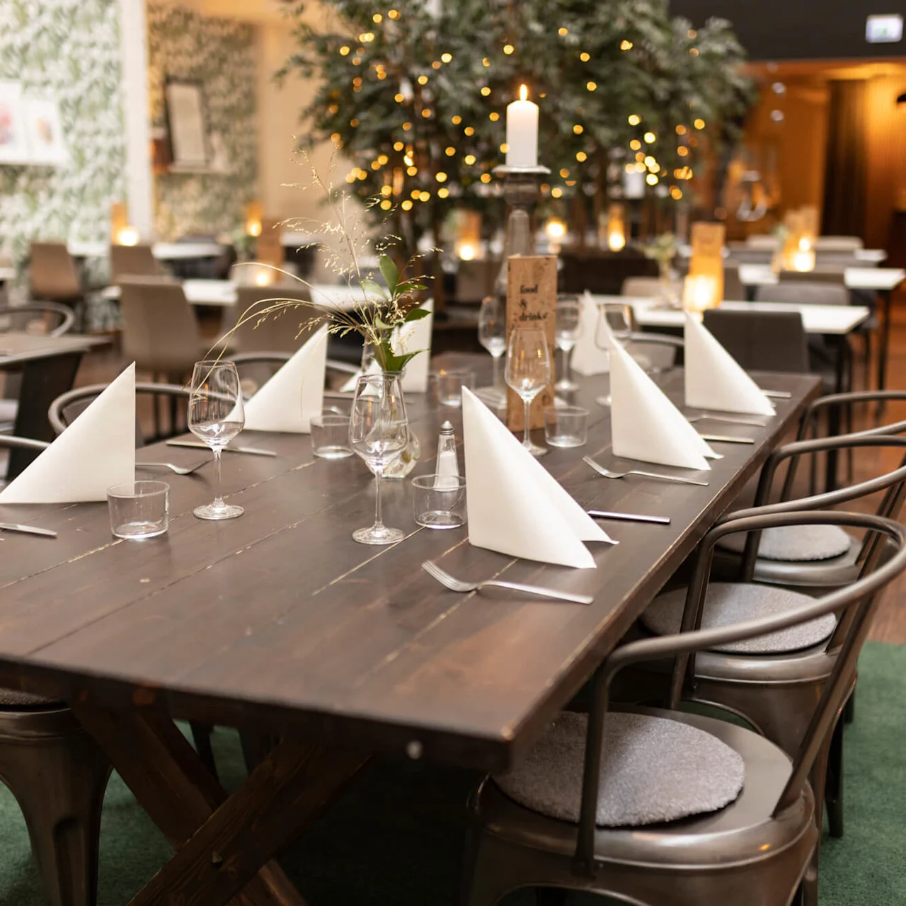 A neatly set dining table in a cozy restaurant with ambient lighting and festive decorations.