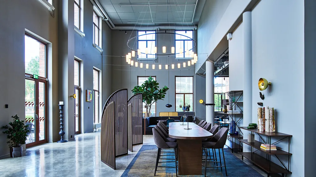 An office lobby with a modern design, polished floors, furnishings, and indoor plants, illuminated by natural and artificial light.
