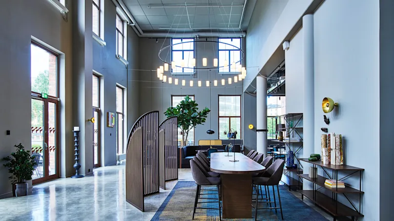 An office lobby with a modern design, polished floors, furnishings, and indoor plants, illuminated by natural and artificial light.