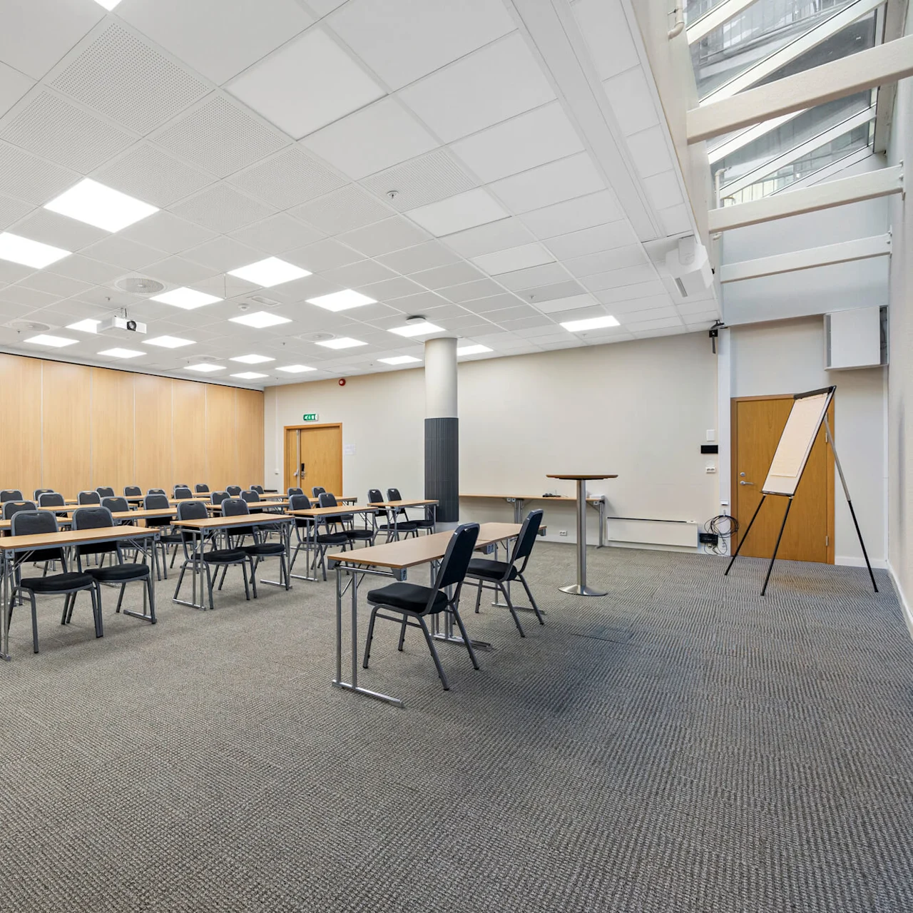 Rows of chairs and tables in a well-lit, empty classroom with a wooden panel wall and a gray carpet.