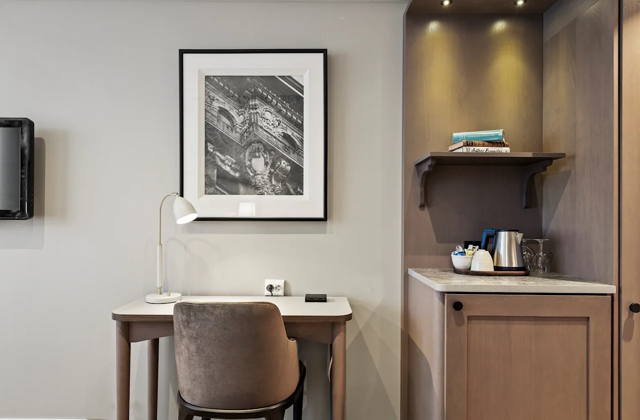 A well-appointed hotel room featuring a comfortable workspace with a desk and lamp, alongside a convenient beverage area.