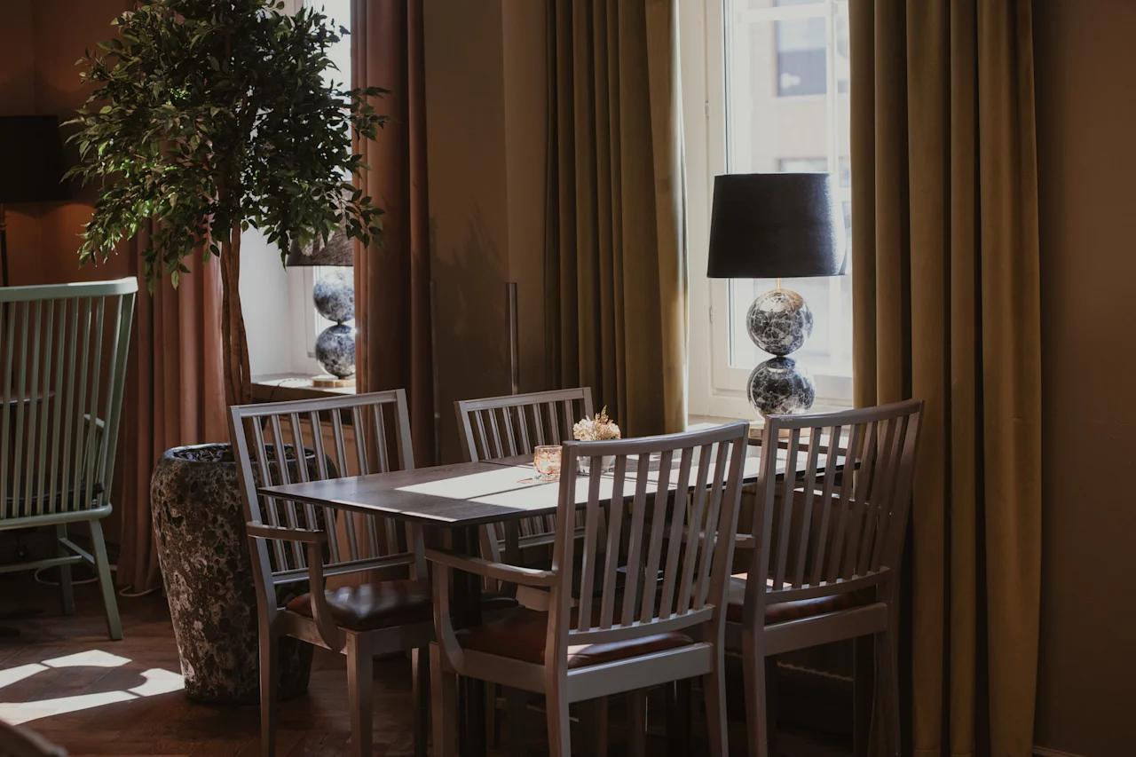 Et koselig spiseområde med et trebord og stoler, opplyst av naturlig lys fra et vindu med gardiner.