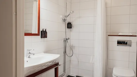 A clean and modern bathroom with a sink, shower, and toilet, featuring a black and white checkered shower floor. Home Hotel Kung Oscar.