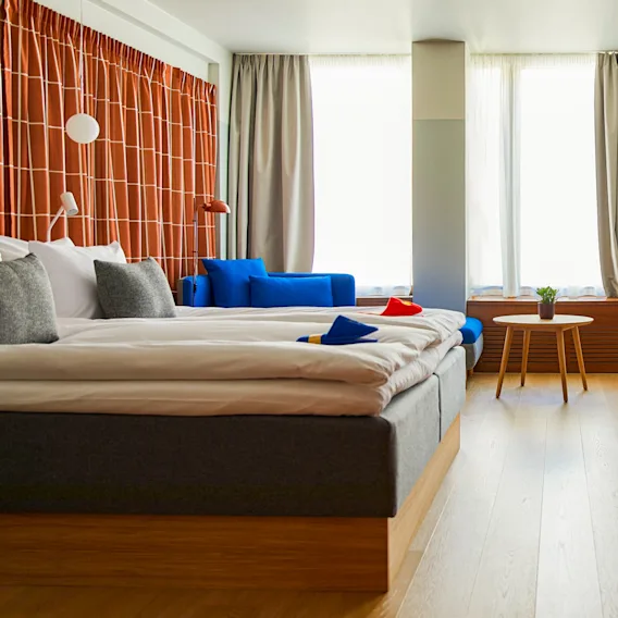 A modern and inviting hotel room with a large bed, blue sofa, and a wall-mounted TV, featuring warm colors.
