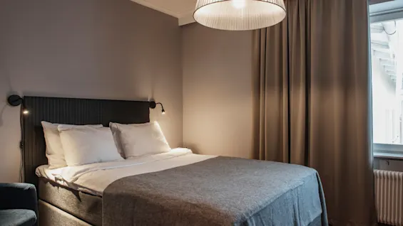 Ett mysigt hotellrum med en bekväm säng, mjuk belysning och varma gardiner, som inbjuder till avkoppling.