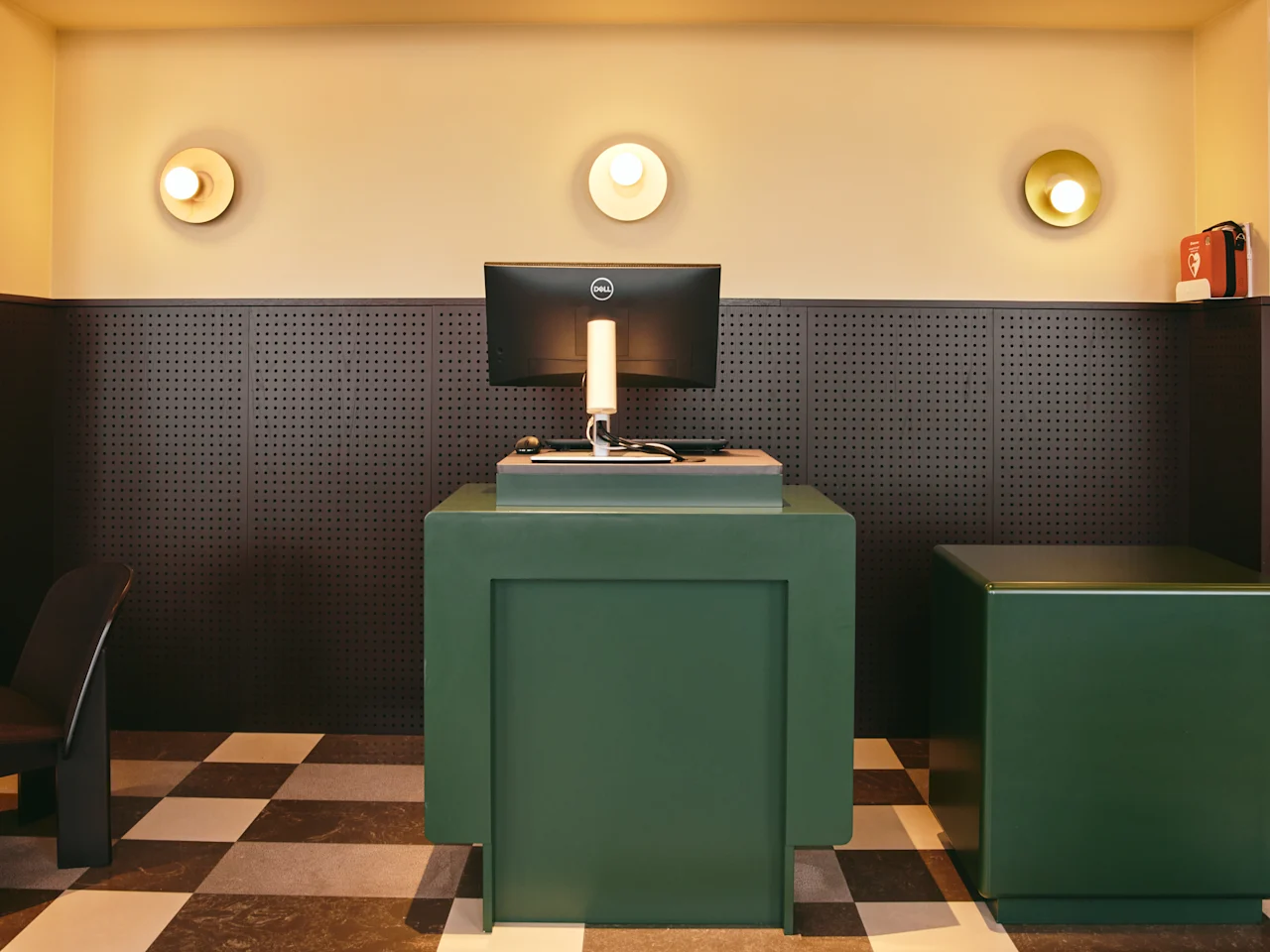 En modern reception med gröna diskar, en dator och cirkulära vägglampor, med ett rutigt golv.