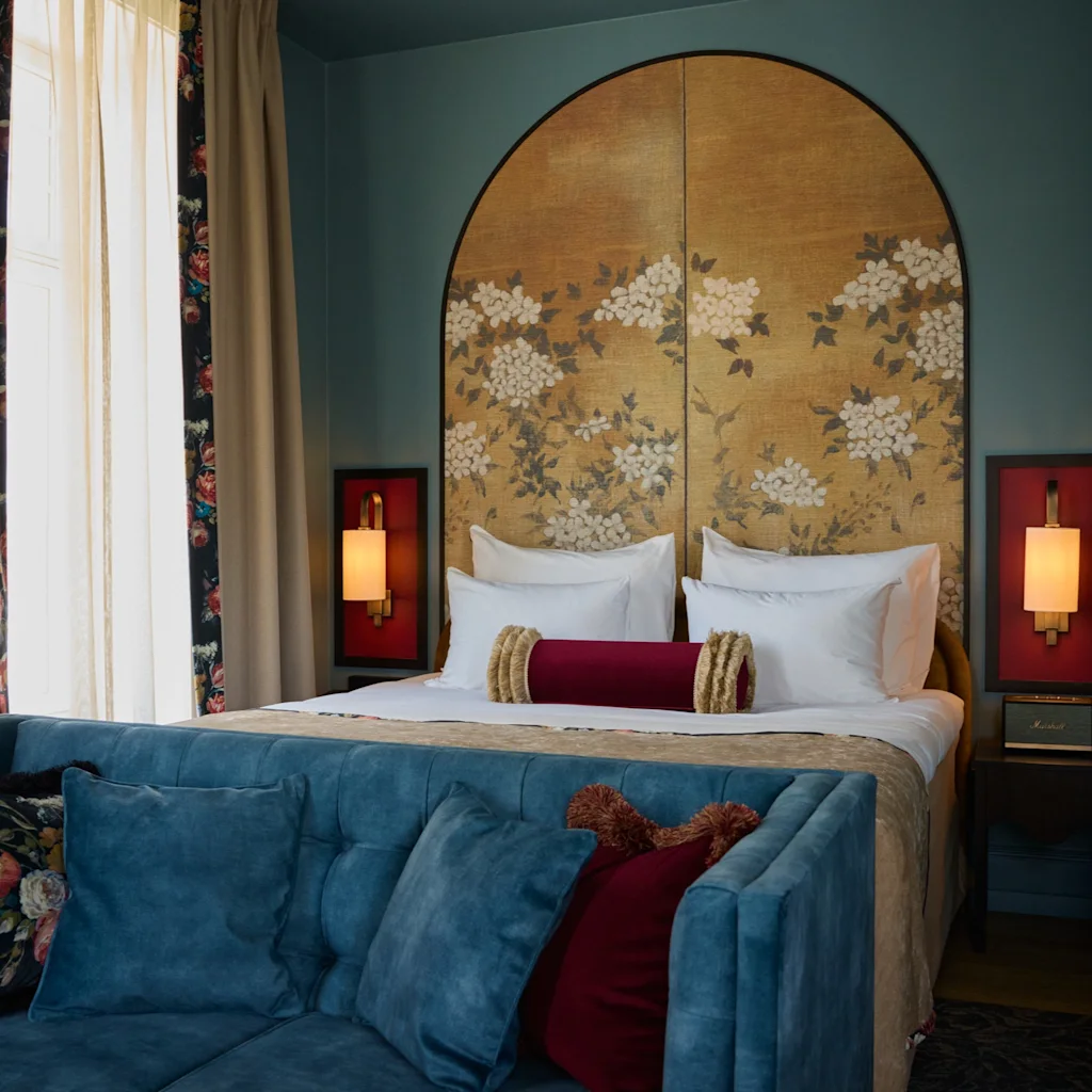 Ett lyxigt hotellrum på Hotel Christiania Teater med en stor säng, blommig sänggavel och en bekväm blå soffa.