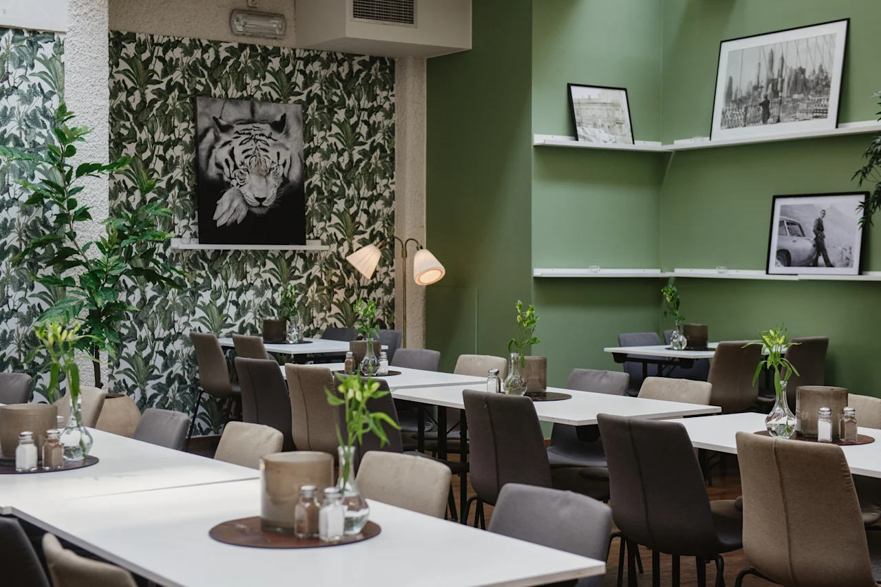 Moderna café med snyggt arrangerade bord och stolar, dekorerade med botanisk tapet och gröna väggar. Svartvitt tigerfotografi och stadslandskapskonstverk ger en visuell intresse till den avslappnade atmosfären.