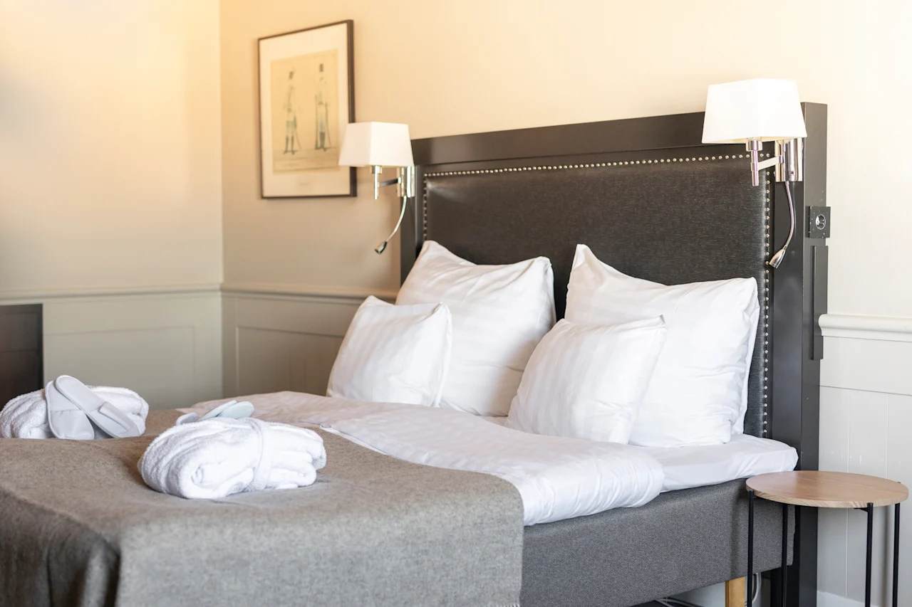 Ett bekvämt hotellrum med en prydligt bäddad säng, vita badrockar och tofflor, vilket antyder en avkopplande vistelse.