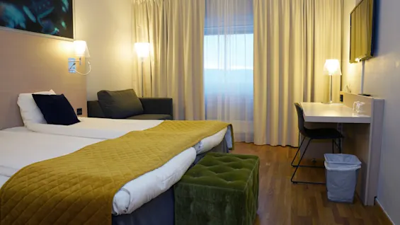 Mukava hotellihuone Quality Hotel Sundsvallissa, jossa on kaksi sänkyä, työpöytä ja viihtyisä oleskelutila ikkunan äärellä.