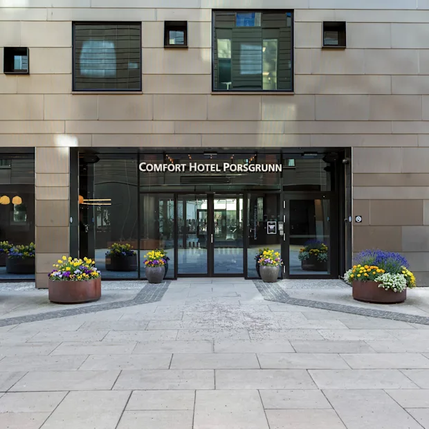 Inngangen til Comfort Hotel Porsgrunn, med glassdører, en moderne fasade og fargerike blomsterpotter.