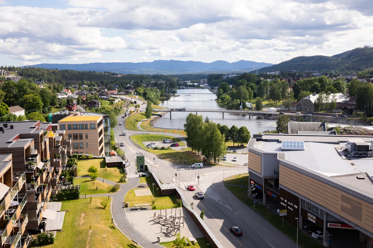 Et luftfoto av en by med en elv som renner gjennom den, omgitt av bygninger, veier og frodige grønne fjell.