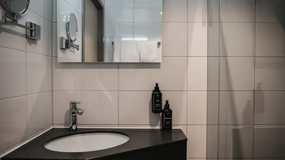 Et godt opplyst baderom med en elegant vask, moderne kran og et stort speil over, med to flasker toalettartikler.