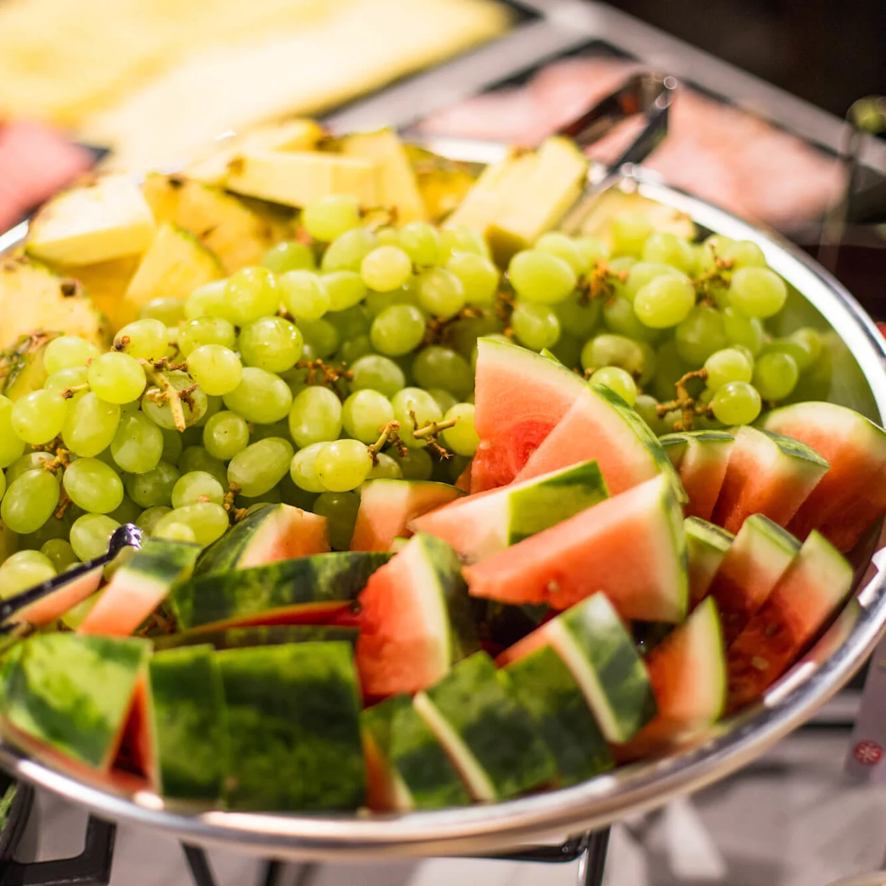 A selection of cheeses and fresh fruit slices displayed on a serving platter, suggesting a buffet or catering event.