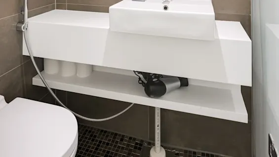En vit handfat med en modern kran håller en blå tvålpump märkta "WHITE RACK." Belägen i ett stiligt, kaklat badrum med spegel, hyllor, handdukar och en hårtork.