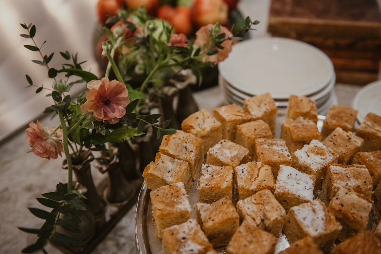 A delightful spread of square cakes, some dusted with sugar, alongside floral arrangements at Home Hotel Baltzar.