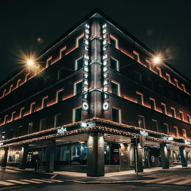 Tiilirakennus yöllä, valaistu katuvaloilla ja koristevaloilla. Kulmassa kyltti HOTEL MESTARI.