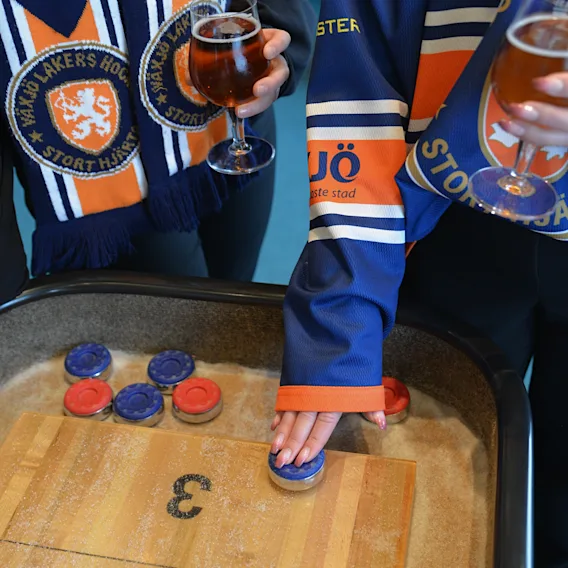 Personer i hockeytröjor som spelar shuffleboard och håller i öl