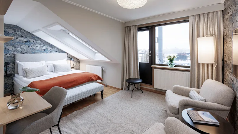 A well-lit attic bedroom with a sloped ceiling, a double bed, and modern decor, featuring a window with a view.