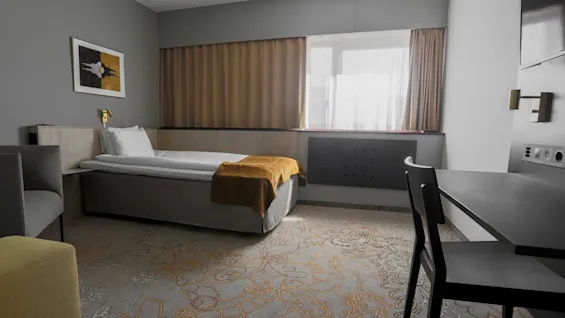 A single bed with a brown throw blanket sits in a modern, minimalistic hotel room. A desk and chair are on the right; a window with curtains lets in light.