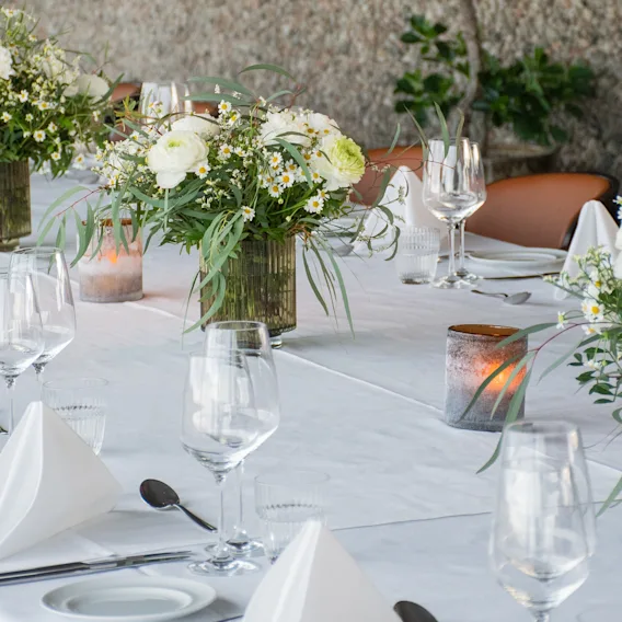 Et vakkert dekket bord for et arrangement, med hvite blomsteroppsatser, levende lys og elegante kuverter.