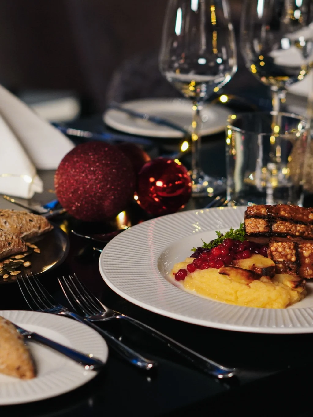 En tallerken med grillet tofu og most squash pyntet med tyttebær står på et pyntet bord med vinglass, brød og julepynt.