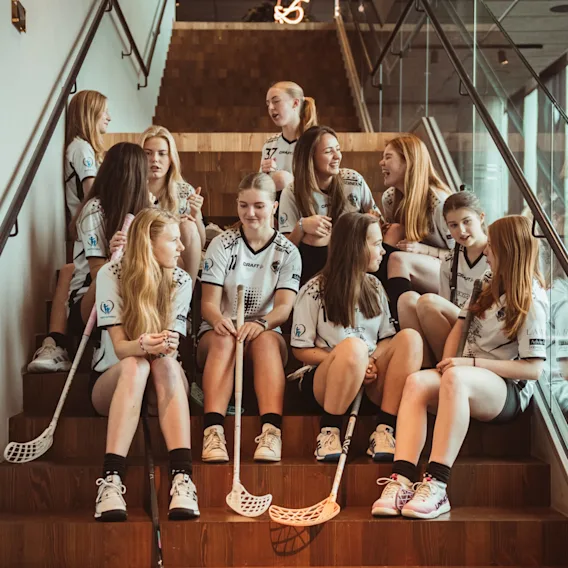 Et innebandylag i uniform slapper av og prater i en moderne tretrapp.