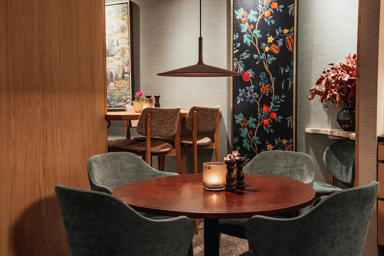 Et hyggeligt spiseområde på Home Hotel Wellington med bord, levende lys, komfortable stole og elegant botanisk kunst.