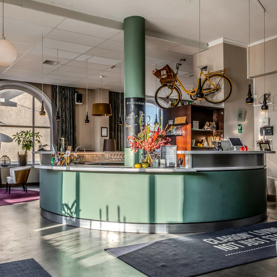 A modern hotel lobby with stylish furniture, a bicycle hanging above the reception desk, in a spacious, well-lit room.