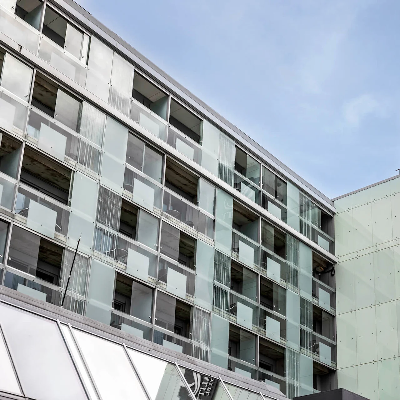 En modern glasbyggnad med skylten "QUALITY HOTEL" reser sig mot en klarblå himmel och betonar urban arkitektur med geometriska linjer och reflekterande paneler.