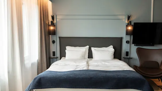 Et koselig hotellrom med en stor seng, myk belysning fra nattbordslamper, en veggmontert TV og en komfortabel lenestol.