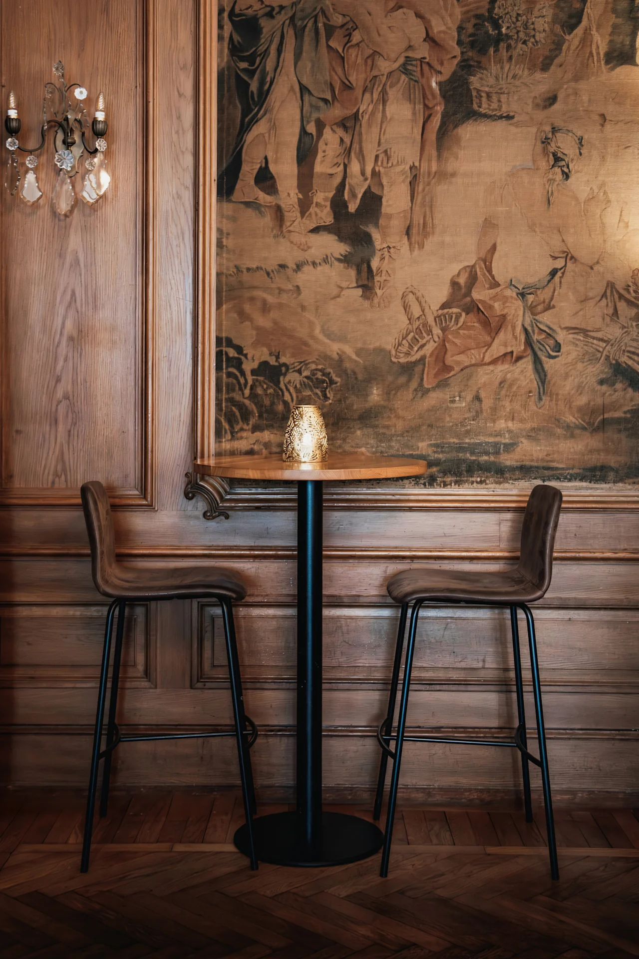 En mysig hörna med ett litet bord och två barstolar, placerad mot en rik gobeläng och träpaneler. Home Hotel Grand, Helsingborg.