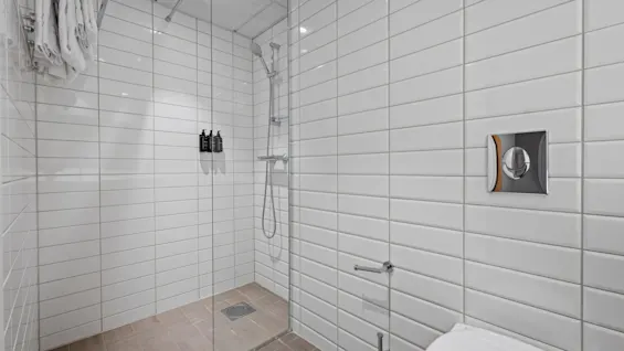 Ett ljust och rent hotellbadrum med vita kaklade väggar, en rymlig duschkabin i glas och en toalett.