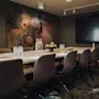 A long conference table with chairs holds pitchers, glasses, and a bowl of green apples. In the room are a large screen and a colorful painting.  