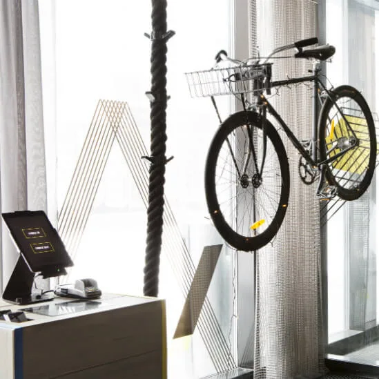 A bicycle hangs on a glass wall inside a modern room with large windows, beside a desk featuring a digital display and card reader.